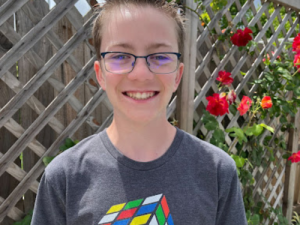 High school student smiles for his photo wearing glasses and a shirt with a Rubik's Cube on it