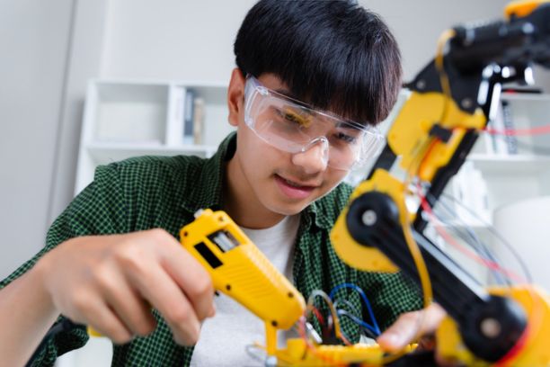 Asian teenager doing robot arm homework project at home, technology of robotics programing and STEM education