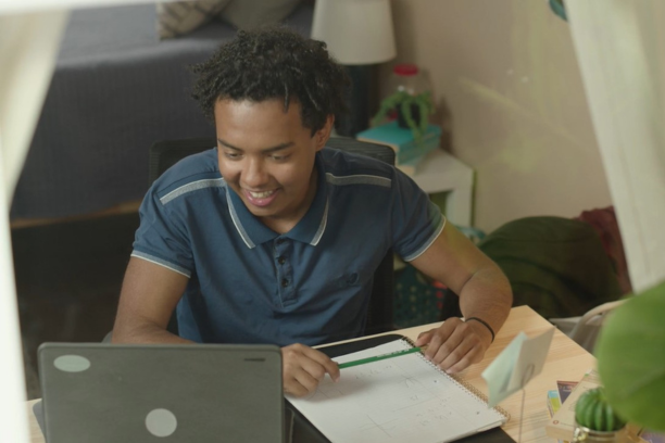 Black high school teen smiles at his Chromebook while working on his studies in his bedroom