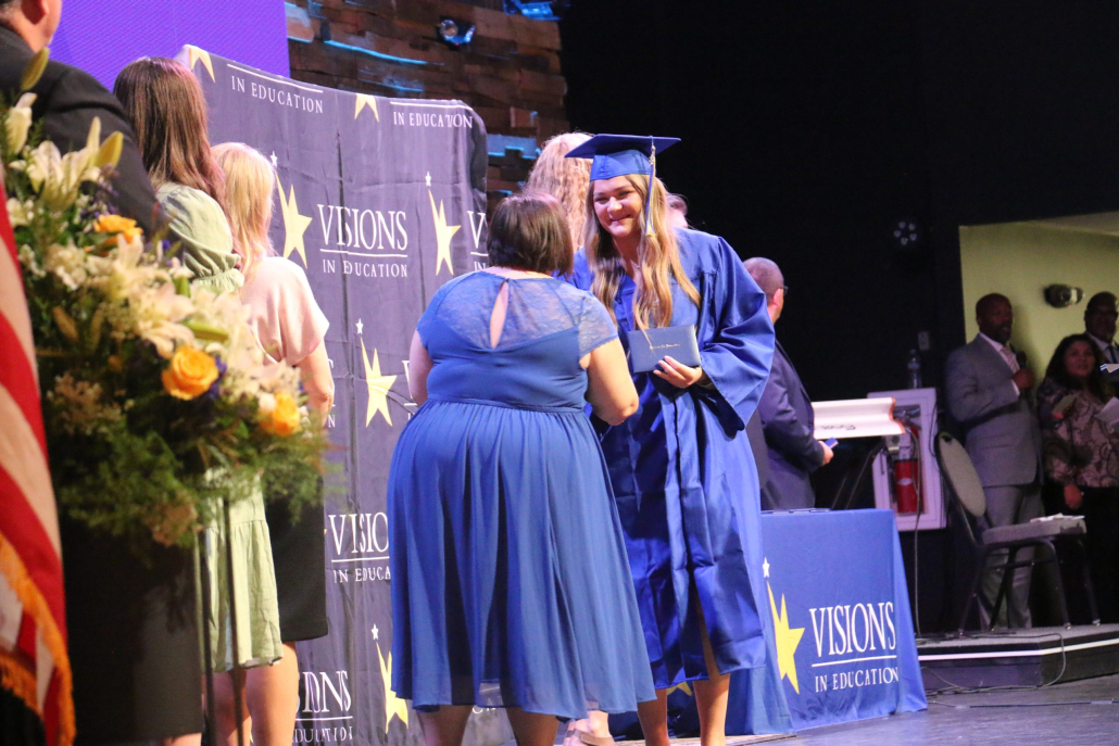 Smiling graduate shakes a staff member's hand on stage as she receives her diploma.
