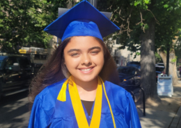 High school girl smiles in bright blue graduation cap and gown wearing yellow tassels at her high school graduation.