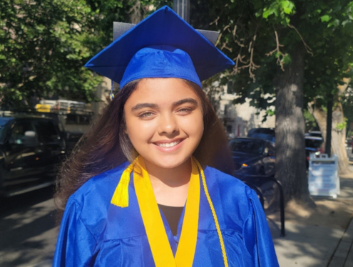 High school girl smiles in bright blue graduation cap and gown wearing yellow tassels at her high school graduation.