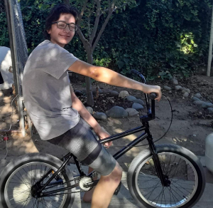 Teenage boy with glasses sits on his bike and turns to smile at the camera.