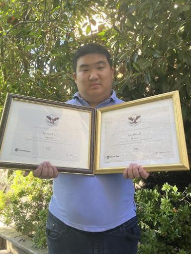 Julian Lau stands holding his two President's Volunteer Service Awards.