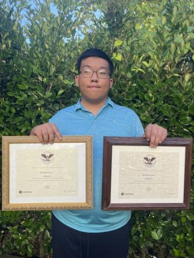 Justin Lau stands holding his two President's Volunteer Service Awards.
