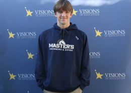 Charley Sears, in a navy The Master's University sweatshirt that reads Master's Swimming and Diving, poses in front of a blue backdrop with Visions In Education logos on it.