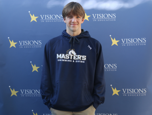 Charley Sears, in a navy The Master's University sweatshirt that reads Master's Swimming and Diving, poses in front of a blue backdrop with Visions In Education logos on it.