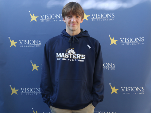 Charley Sears, in a navy The Master's University sweatshirt that reads Master's Swimming and Diving, poses in front of a blue backdrop with Visions In Education logos on it.
