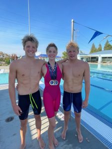 Charley stands next to his sister, Kaylee, and brother, JT next to a competitive swimming pool.