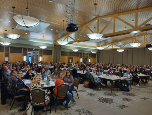 Over 250 Visions staff sits around multiple tables in a big community center room and smiles for a group photo.