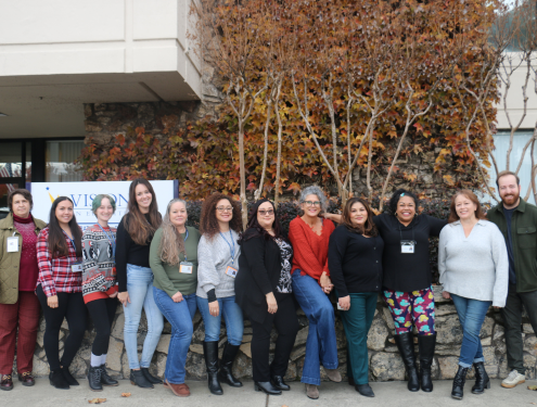 All instructional support staff, including Office Coordinators, Charter School Secretaries and Administrative Assistants, stand together in a line in front of Visions' office building.