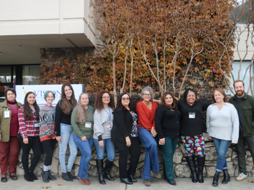 All instructional support staff, including Office Coordinators, Charter School Secretaries and Administrative Assistants, stand together in a line in front of Visions' office building.