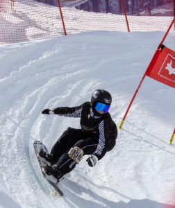 Jax cruises around a red flag in the snow in full snowboarding gear.