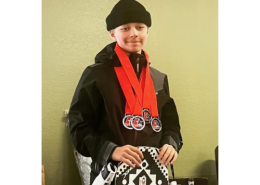 Jax Allen poses with his snowboard wearing a black beanie, black jacket, and multiple red medals around his neck.