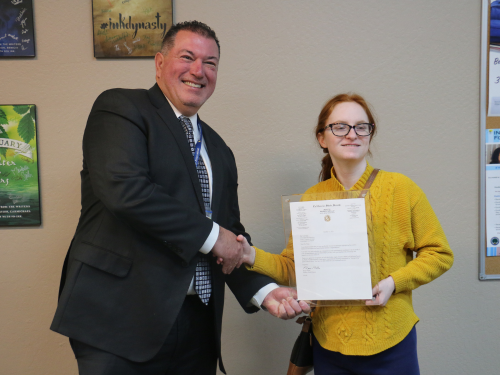 Superintendent Olmos stands next to Tori Berg in the Learning Center, holding the framed letter from Senator Niello in one hand and shaking Tori's hand with the other.