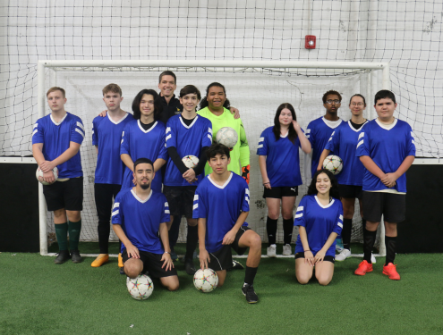 Visions' club soccer team huddles together in front of a soccer goal post for a team photo.