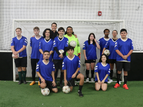 Visions' club soccer team huddles together in front of a soccer goal post for a team photo.