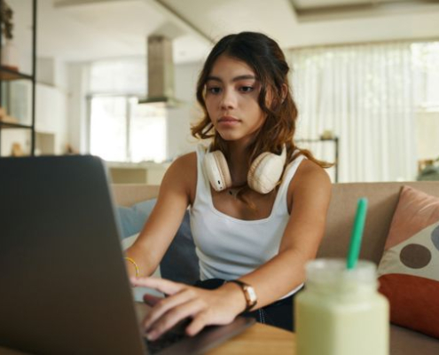 Serious teenage girl with headphones working on laptop on her online high school cybersecurity college class