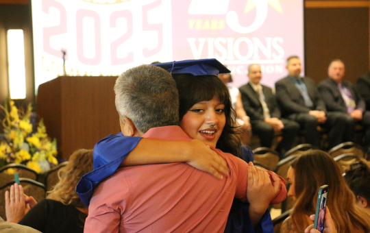 Visions graduate in cap and gown hugging a family member.