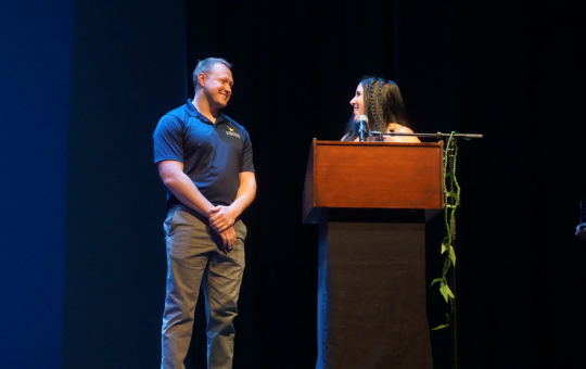 Photo of Alumni Hall of Fame Inductee Tanner Zumwalt and his former Visions teacher on stage at the August staff back to school event.