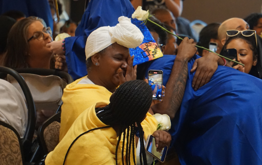 Visions graduate in cap and gown hugging a family member.