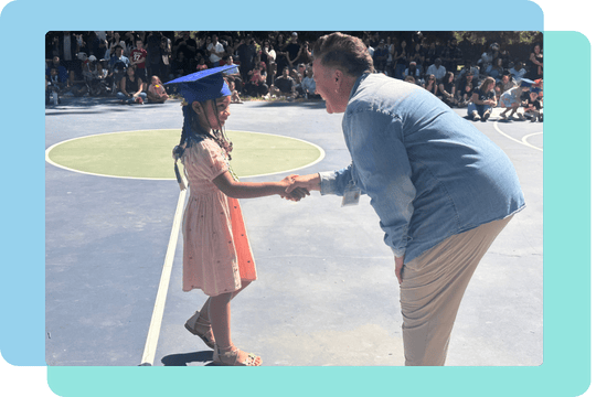 Principal shaking young student in graduation cap's hand.