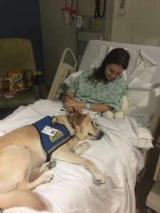 Visions student in hospital bed with a therapy dog.