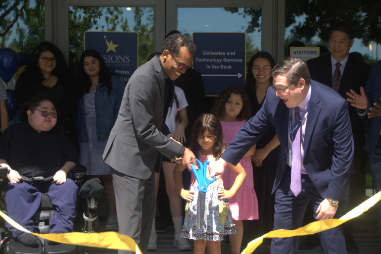 Two Board members cut gold ribbon with large blue scissors.