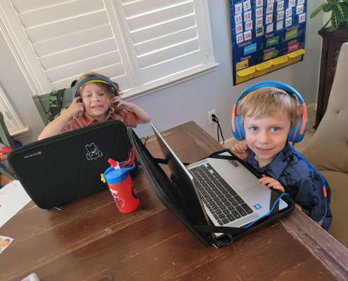 Two young students wearing headphones, sitting at a table with their laptops
