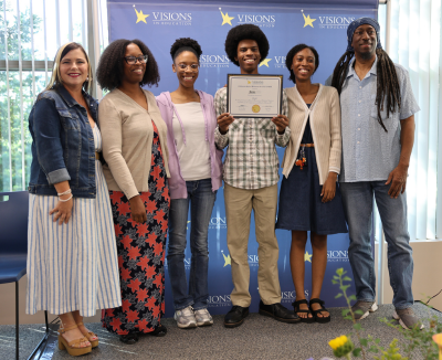 A State Seal of Biliteracy earner poses for a group photo with his family and Visions teacher.