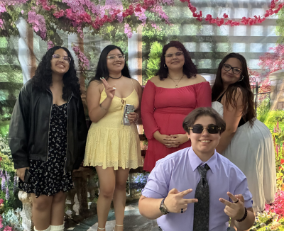 A group of students gather for a group picture in front of a floral backdrop.