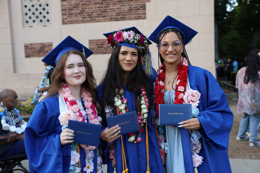 A group of three Visions graduates pose for a photo in front of Memorial Auditorium holding their diplomas.
