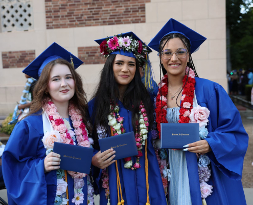 A group of three Visions graduates pose for a photo in front of Memorial Auditorium holding their diplomas.