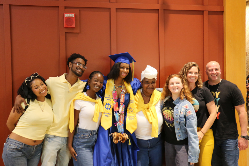 A Visions summer graduate in a blue cap and gown poses with her family for a group photo.