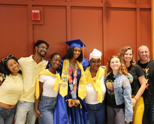 A Visions summer graduate in a blue cap and gown poses with her family for a group photo.
