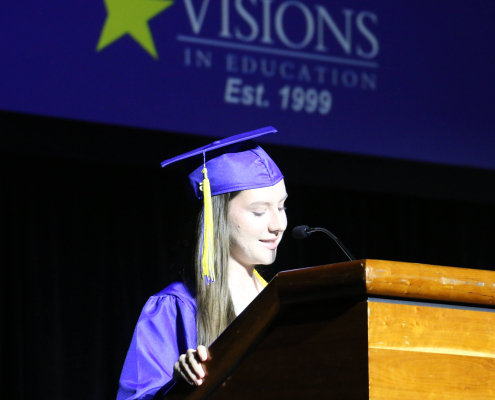A Visions graduate stands at a podium in her cap and gown and delivers a speech at Visions' graduation ceremony.