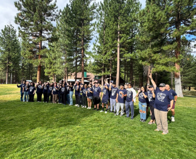 Visions student campers all gather on a lawn in the forest wearing matching camp t-shirts.