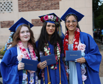 A group of three Visions graduates pose for a photo in front of Memorial Auditorium holding their diplomas.