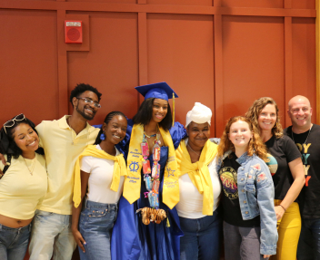 A Visions summer graduate in a blue cap and gown poses with her family for a group photo.