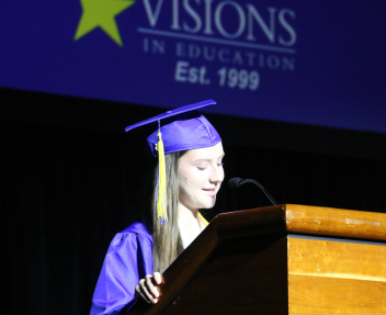 A Visions graduate stands at a podium in her cap and gown and delivers a speech at Visions' graduation ceremony.