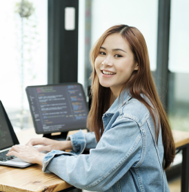Young programmer or IT specialist satisfied with her work done. Happy young woman working on laptop while sitting at her working place in office.