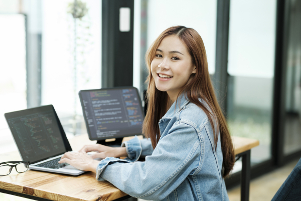 Young programmer or IT specialist satisfied with her work done. Happy young woman working on laptop while sitting at her working place in office.