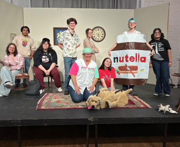 A group of students in costume pose on stage with their drama teacher after their production of “An Absolutely True Story (As Told by a Bunch of Lying Liars)”
